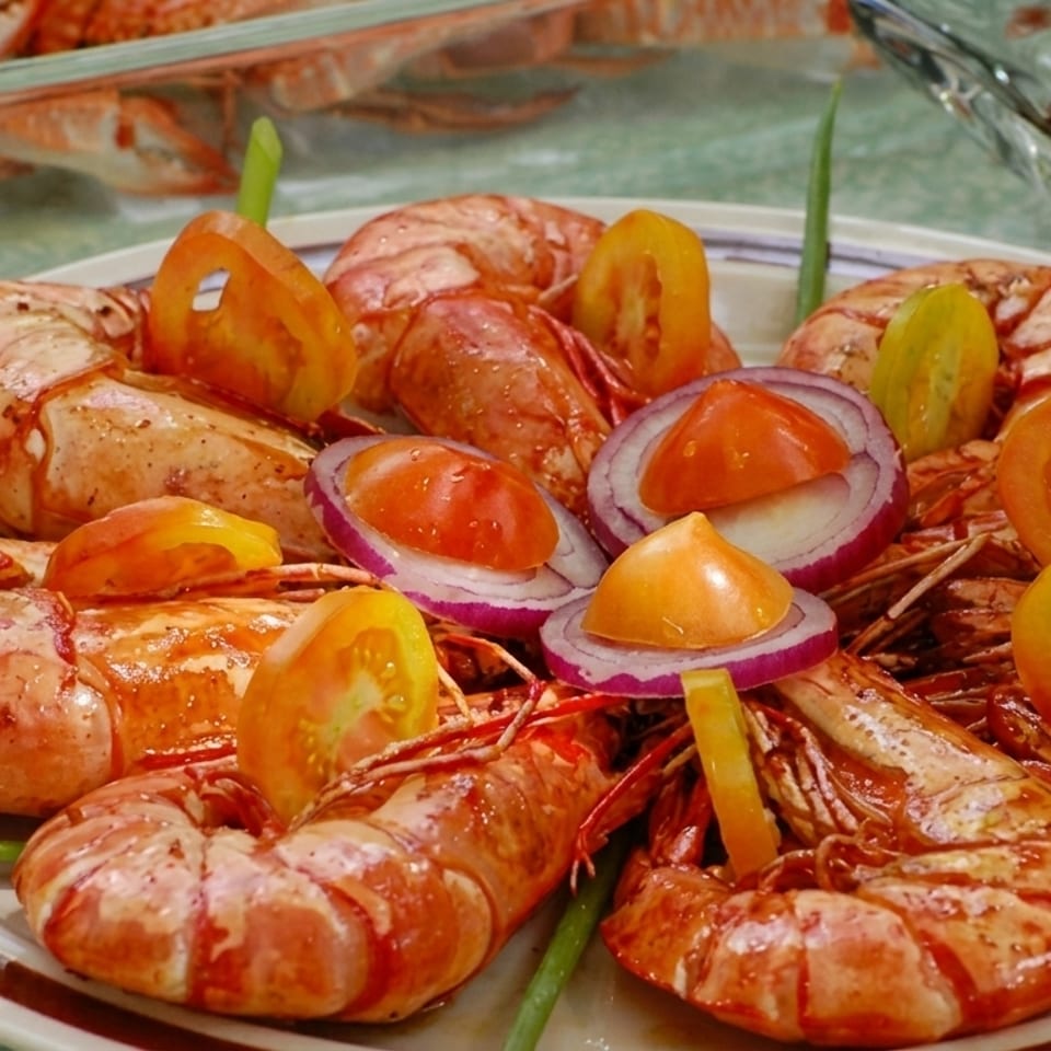 A platter of cooked shrimp garnished with sliced tomatoes, red onions, and green onions.